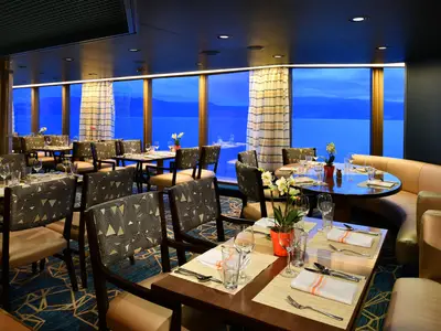 Gedeckte Tische in einem eleganten Restaurant an Bord der Westerdam mit großen Panoramafenstern zum blauen Meer.