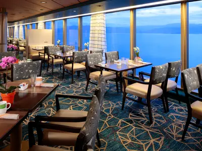Gedeckte Tische im Lido Restaurant an Bord der Westerdam mit großen Panoramafenstern und Blick auf das blaue Meer.