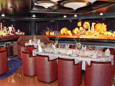 Elegant eingedeckte Tische und rote Sessel im Pinnacle Grill Restaurant an Bord der Westerdam vor großen herbstlichen Gemälden.
