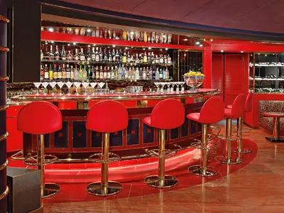 Die rot-goldene Pinnacle Grill Bar an Bord der Westerdam mit eleganten Barhockern und einer großen Auswahl an Getränken.