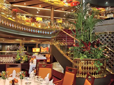 Elegantes Restaurant mit geschwungener Treppe, goldenen Geländern und eingedeckten Tischen an Bord der Westerdam.