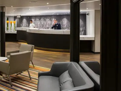 Die Rezeption an Bord der Westerdam mit Mitarbeitern am Counter und bequemen Sesseln im Vordergrund.