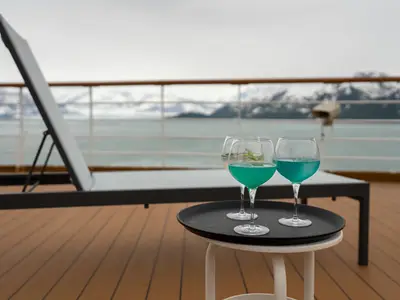 Drei Cocktails auf einem Tablett an Bord der Westerdam mit Blick auf eisige Berge in Alaska.