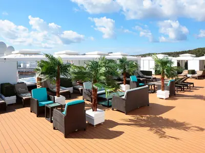 Blick auf den exklusiven Sonnendeck-Bereich The Retreat an Bord der Westerdam mit Sonnenliegen, Cabanas und kleinen Palmen unter blauem Himmel.