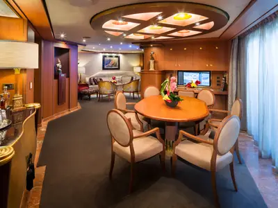 Blick in eine großzügige Suite an Bord der Westerdam mit rundem Esstisch, Holzvertäfelung, Bar und gemütlicher Sitzecke im Hintergrund.