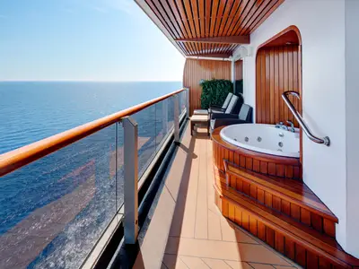 Balkon einer Suite an Bord der Westerdam mit privatem Whirlpool, Holzverkleidung, Liegestühlen und Meerblick.