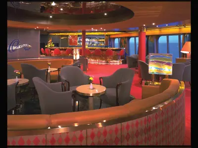 Blick in die elegant eingerichtete Ocean Bar an Bord der Zaandam mit Sesseln, Barhockern und Meerblick.