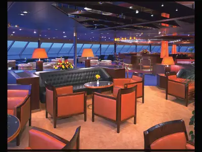 Elegante Bar-Lounge an Bord der Zaandam mit bequemen Ledersesseln, stimmungsvoller Beleuchtung und Panoramafenstern zum Meer.