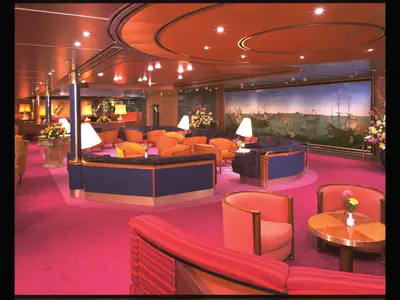 Die Explorer's Lounge an Bord der Zaandam mit pinkfarbenem Teppich, gemütlichen Sesseln und einem großen Gemälde.