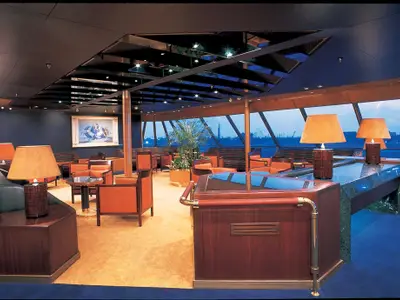 Die gemütliche Crow's Nest Lounge an Bord der Zaandam mit Sesseln, warmen Lampen und Panoramafenstern.