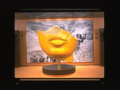 Blick auf eine leuchtend gelbe Gesichtsskulptur in einer Ausstellung an Bord der Zaandam vor einer historischen Schwarz-Weiß-Fotografie.