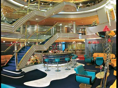 Blick in das elegant gestaltete Atrium an Bord der Zuiderdam mit geschwungenen Treppen, der Ocean Bar und türkisfarbenen Sesseln.