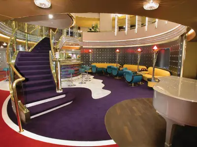 Blick auf das elegant gestaltete Atrium an Bord der Zuiderdam mit violetter Auslegeware, einer goldenen Wendeltreppe und gemütlichen Sitzbereichen.