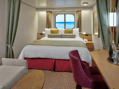 Blick in eine gemütliche Außenkabine an Bord der Zuiderdam mit Doppelbett, Sessel und Fenster zum Meer.