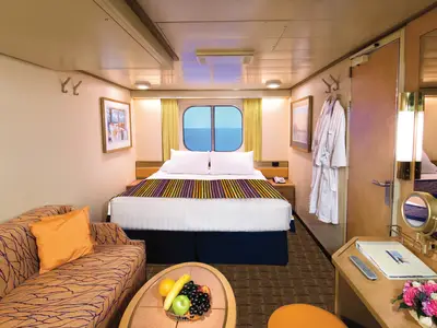 Eine gemütliche Außenkabine an Bord der Zuiderdam mit einem Doppelbett vor einem runden Fenster mit Meerblick, einem Sofa und Bademänteln.