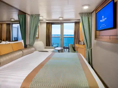 Eine gemütliche Balkonkabine an Bord der Zuiderdam mit Doppelbett, Sofa, TV und Blick durch die Balkontür auf das blaue Meer.