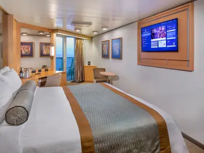 Eine geräumige Balkonkabine an Bord der Zuiderdam mit einem großen Bett, Fernseher, Sitzecke und Zugang zum privaten Balkon mit Meerblick.