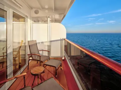 Balkon an Bord der Zuiderdam mit bequemen Möbeln und einer Glasreling, die den Blick auf das weite, blaue Meer freigibt.