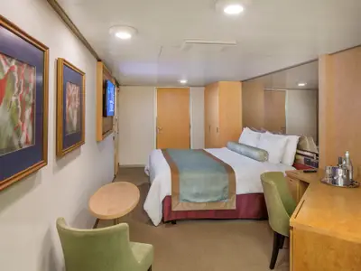 Einblick in eine stilvolle Kabine an Bord der Zuiderdam mit einem großen Bett, Spiegelwand, Holzmöbeln und zwei grünen Sesseln.