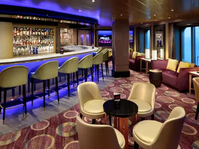 Elegante Bar an Bord der Zuiderdam mit blau beleuchtetem Tresen, beigen Barhockern und gemütlichen lila Sofas.
