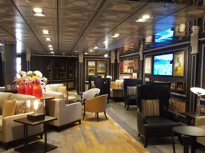 Blick in die stilvoll eingerichtete Gallery Bar an Bord der Zuiderdam mit bequemen Sesseln, Kunstwerken an den Wänden und warmer Beleuchtung.