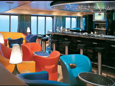 Blick in die moderne, farbenfrohe Sports Bar an Bord der Zuiderdam mit bunten Sesseln, Barhockern und Monitoren.