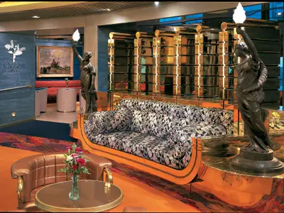Die prunkvolle Ocean Bar an Bord der Zuiderdam mit einem gemusterten Sofa vor einer goldenen Wand und klassischen Statuen.