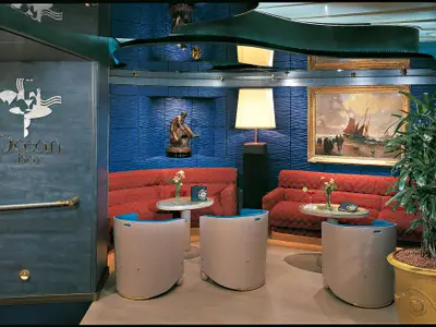 Die stilvolle Ocean Bar an Bord der Zuiderdam mit roten Sofas, beigen Sesseln, blauen Wänden und maritimer Dekoration.