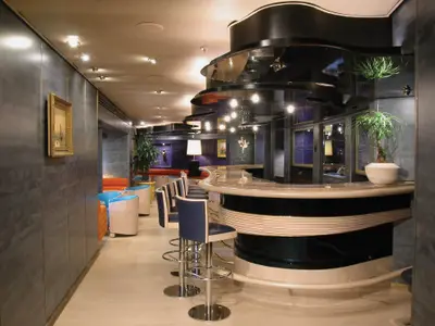 Die elegant gestaltete Ocean Bar an Bord der Zuiderdam mit einer geschwungenen Theke, blauen Sesseln und warmer Beleuchtung.