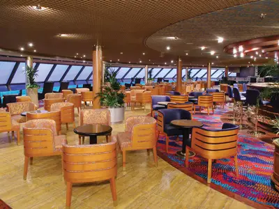 Gemütliche Sessel und Tische in der Crow's Nest Lounge an Bord der Zuiderdam, mit Blick durch große Panoramafenster.