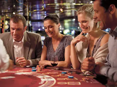 Eine Gruppe gut gelaunter Gäste beim Blackjack-Spiel im Casino an Bord der Zuiderdam mit Jetons und Rotwein.