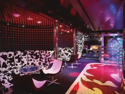 Blick in den farbenfroh beleuchteten Northern Lights Night Club an Bord der Zuiderdam mit markanten Kuhfell-Sesseln und roter Lichtwand.