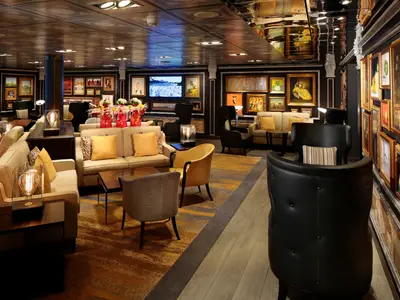 Eine elegant eingerichtete Lounge an Bord der Zuiderdam mit zahlreichen Gemälden an den Wänden und gemütlichen Sesseln.