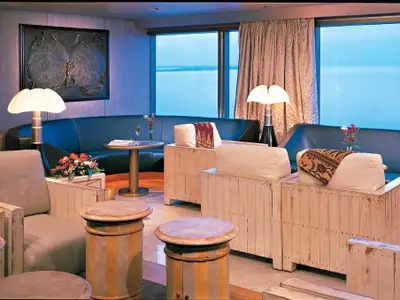 Stilvolle Lounge an Bord der Zuiderdam mit gemütlichen Sesseln, einem Sofa und großen Fenstern mit Blick auf das weite Meer.