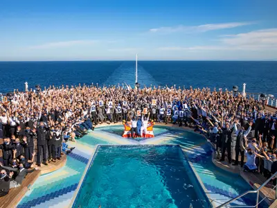 Ein großes Gruppenfoto der Besatzung an Bord der Zuiderdam am Sea View Pool auf dem Außendeck, im Hintergrund das weite Meer.