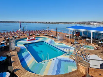 Der Sea View Pool an Bord der Zuiderdam mit blauem Wasser, Whirlpools und Sonnenliegen unter blauem Himmel.