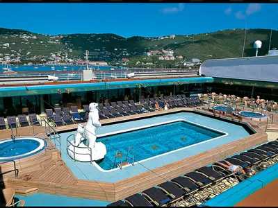 Der Lido-Pool an Bord der Zuiderdam mit einer großen Eisbären-Skulptur, Liegestühlen und Whirlpools vor einer grünen Hügellandschaft.