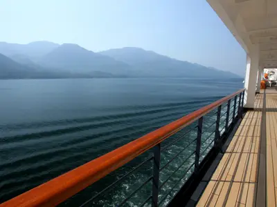 Blick entlang des Holzdecks der Zuiderdam auf das ruhige Meer und die nebligen Berge von Alaska.