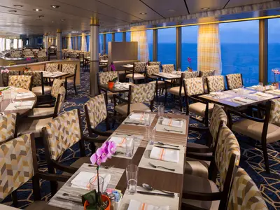 Eingedeckte Tische und gemusterte Sessel im Restaurant an Bord der Zuiderdam mit Blick auf das Meer.