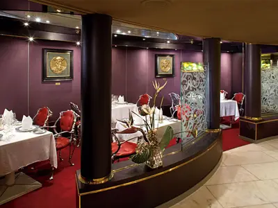 Elegantes Restaurant Pinnacle Grill an Bord der Zuiderdam mit rot bezogenen Stühlen, weißen Tischen, Säulen und lila Wänden.