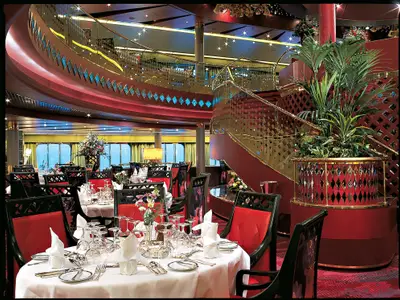 Eingedeckte Tische und eine geschwungene rote Treppe im stilvollen Restaurant an Bord der Zuiderdam.