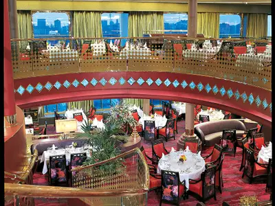 Blick in das elegante, zweistöckige Restaurant an Bord der Zuiderdam mit rot eingedeckten Tischen und goldener Galerie.