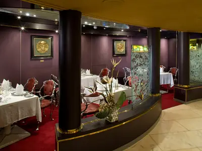 Elegantes Restaurant Pinnacle Grill an Bord der Zuiderdam mit weiß eingedeckten Tischen, roten Stühlen und lila Wänden.