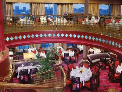 Blick auf den eleganten Vista Dining Room an Bord der Zuiderdam mit zwei Ebenen, weiß gedeckten Tischen und roter Dekoration.