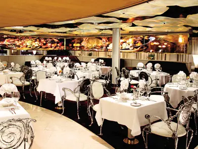 Elegantes Restaurant Pinnacle Grill an Bord der Zuiderdam mit prunkvollen Stühlen, weißen Tischtüchern und einer kunstvollen Deckenbeleuchtung.