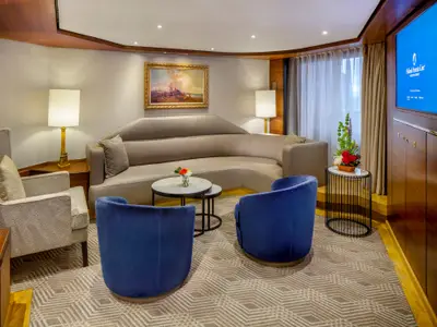 Der elegante Wohnbereich der Pinnacle Suite an Bord der Zuiderdam mit einem grauen Sofa, zwei blauen Sesseln und einem kleinen Tisch.