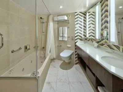 Elegantes Badezimmer einer Signature Suite an Bord der Zuiderdam mit einer Badewanne, Toilette und einem Doppelwaschtisch vor gemusterten Fliesen.