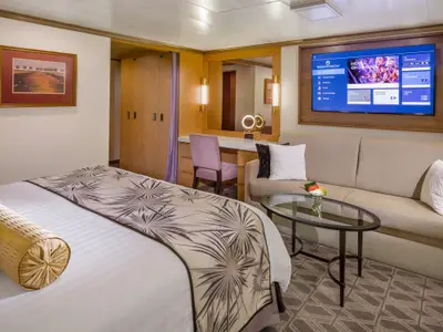 Blick in die gemütliche Signature Suite an Bord der Zuiderdam, ausgestattet mit einem bequemen Sofa, Glastisch, Bett und Flachbildfernseher.
