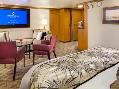 Ein Blick in die stilvolle Neptune Suite an Bord der Zuiderdam mit Sitzecke, Fernseher und dem Bett im Vordergrund.