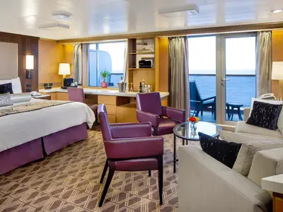 Großzügige Neptune Suite an Bord der Zuiderdam mit großem Bett, lila Sesseln, Sitzbereich und Balkon mit Meerblick.